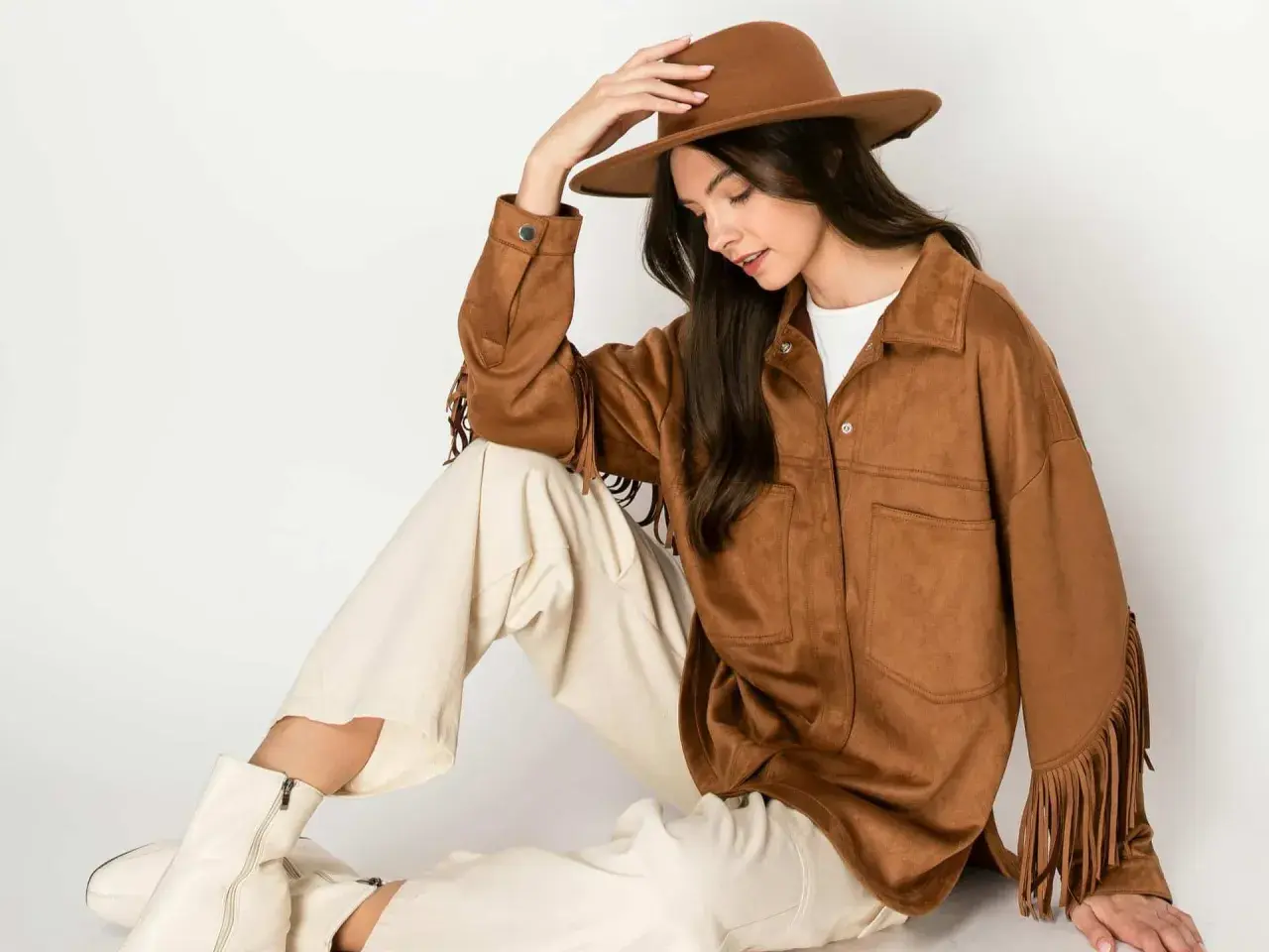 Mujer con sombrero y chaqueta de serraje que es suave y con flecos. Pantalones crema y botas blancas completan el look.