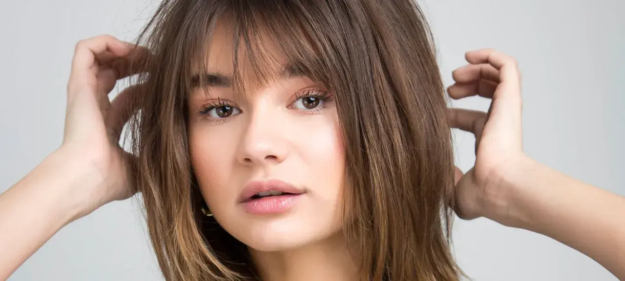 Chica con flequillo desfilado y cabello castaño, ideal para cortes de pelo para cara redonda.