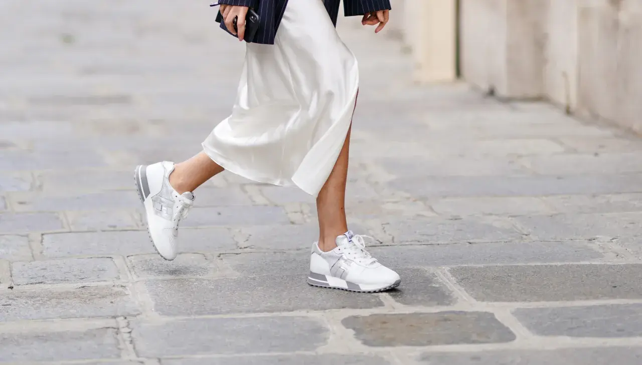 Elegante outfit: vestido blanco satinado con zapatillas deportivas blancas y plateadas.