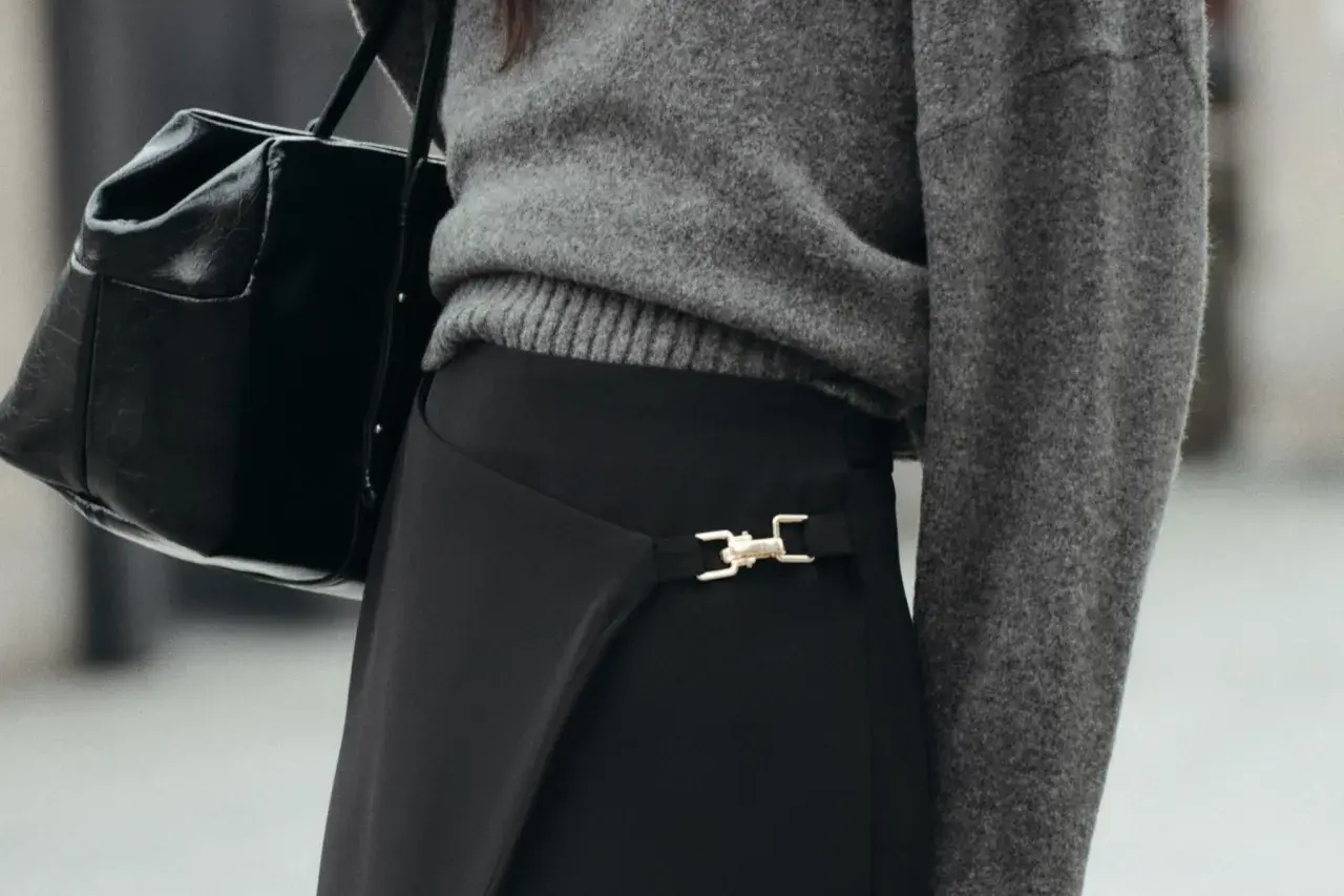 Chaqueta gris y bolso negro sobre falda negra larga con detalle dorado. Un look elegante para saber como combinar una falda negra larga.