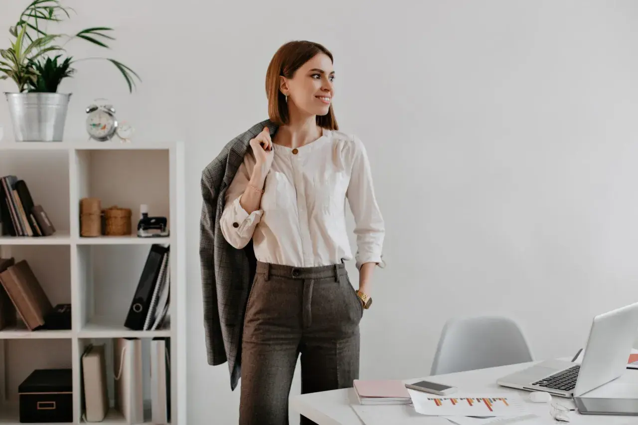 Mujer con un elegante outfit oficina: camisa blanca, pantalón gris y chaqueta a cuadros.