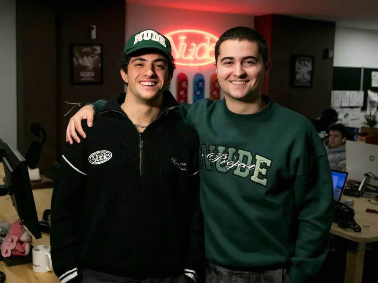 Los fundadores de Nude Project posan sonrientes, uno con gorra verde y el otro con sudadera, ambos luciendo la marca.