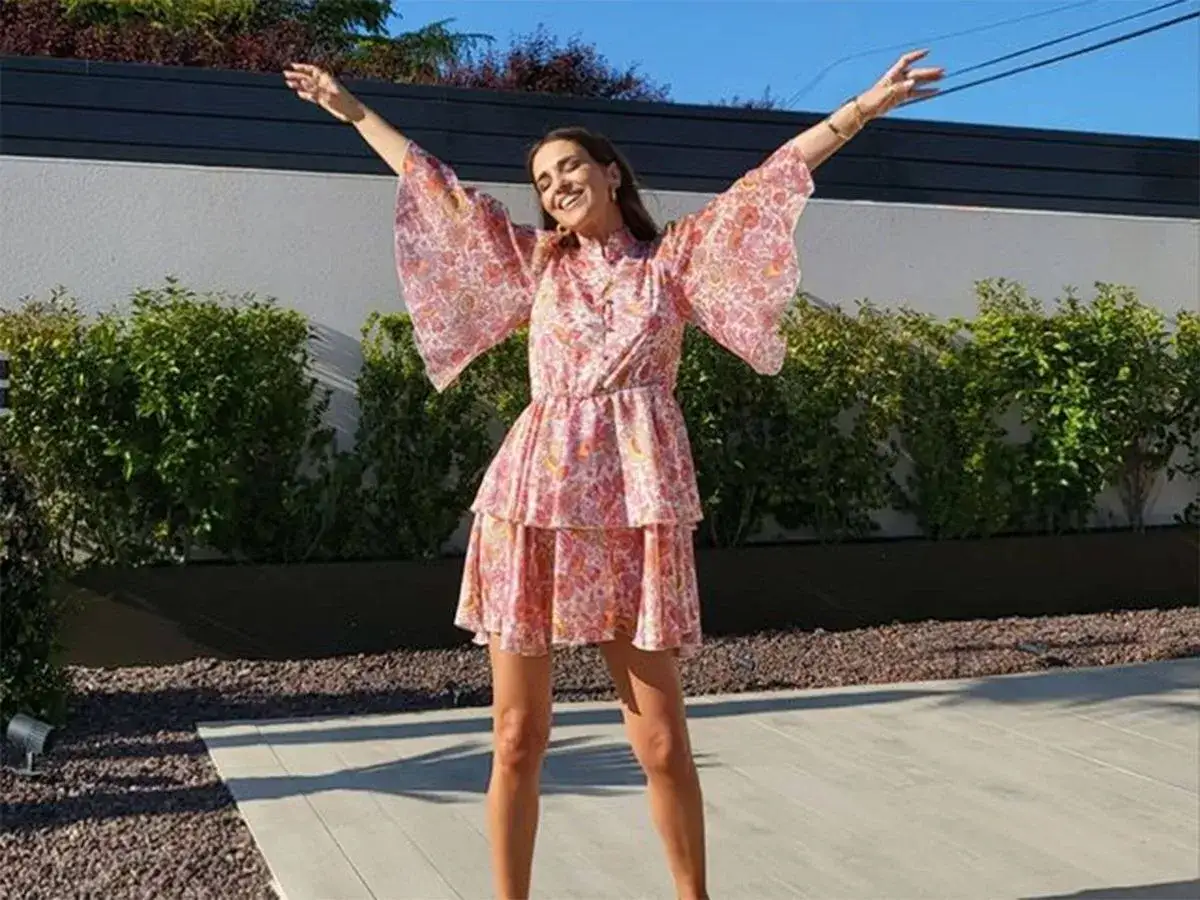 Paula Echevarría luce un vestido rosa con estampado floral y mangas acampanadas, con los brazos extendidos en señal de alegría.