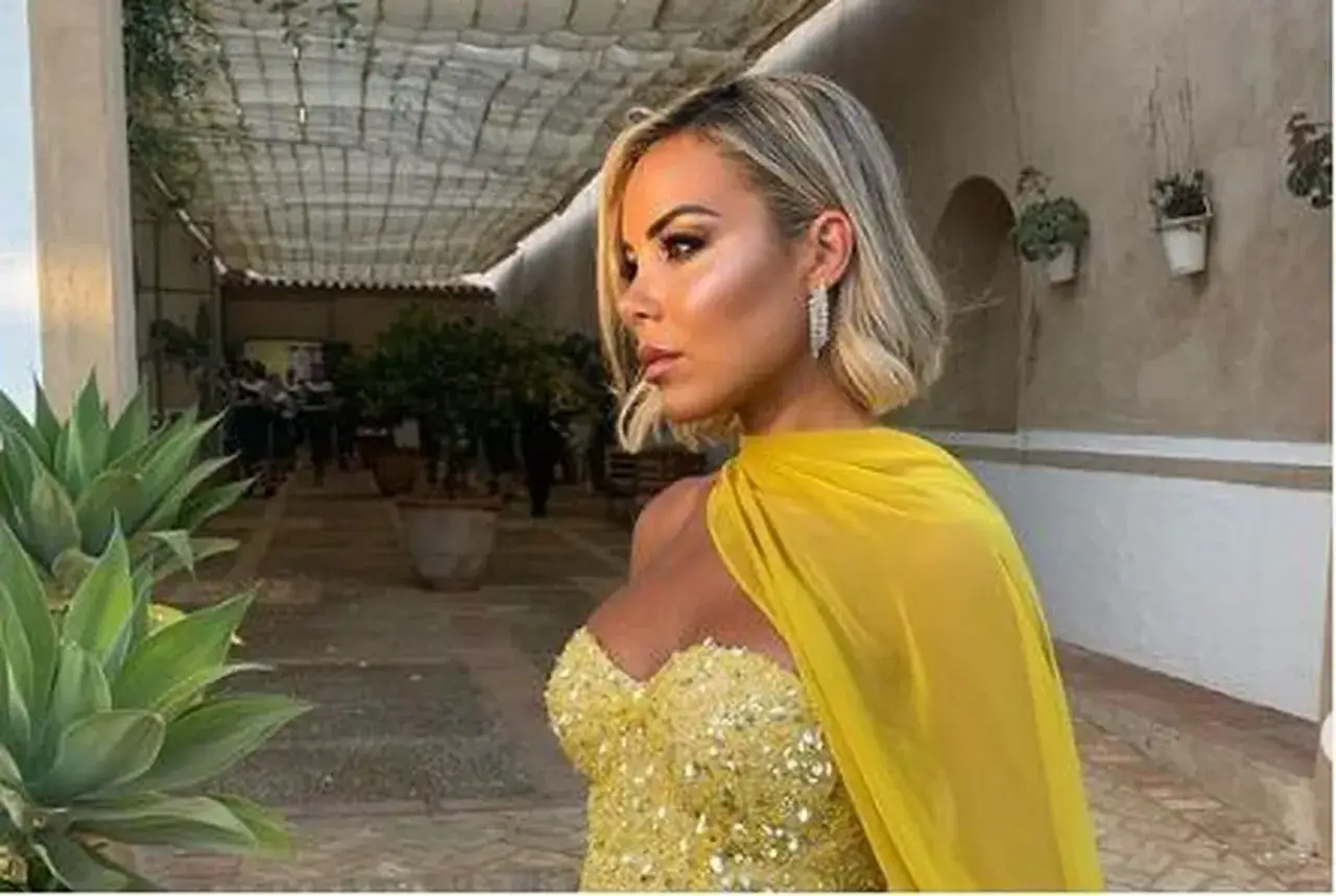 Alba Silva, deslumbrante con un vestido amarillo brillante y capa, posa con elegancia en un patio con plantas.