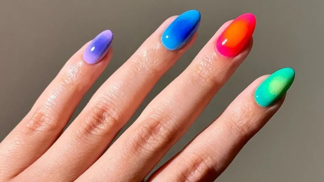 Manicura con aura nails degradadas en tonos morado, azul, naranja neón y verde.
