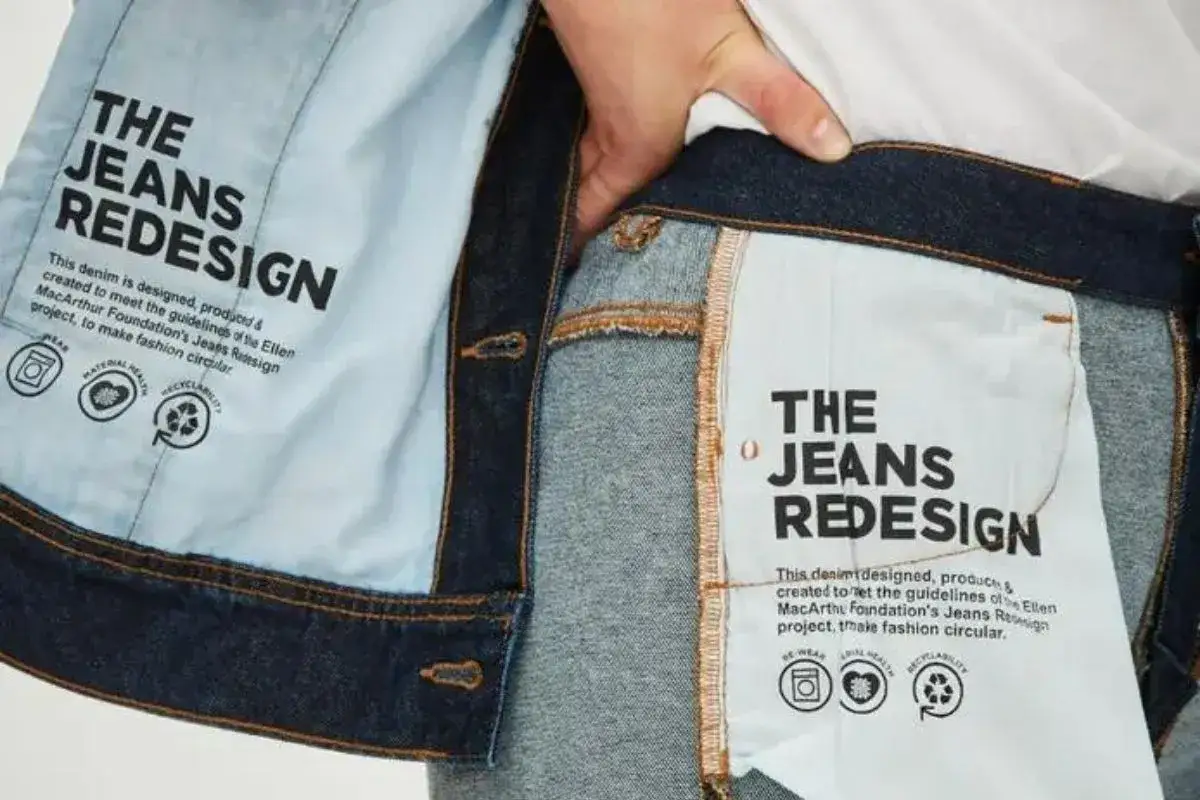 Detalle de etiqueta interior de vaqueros que promueve una marca sostenible y la moda circular, con iconos de reutilización y reciclaje.