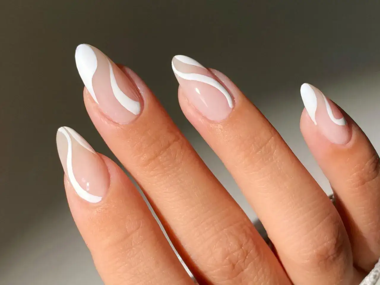 Manos con uñas naturales bonitas, decoradas con un diseño de líneas blancas curvas sobre una base nude.