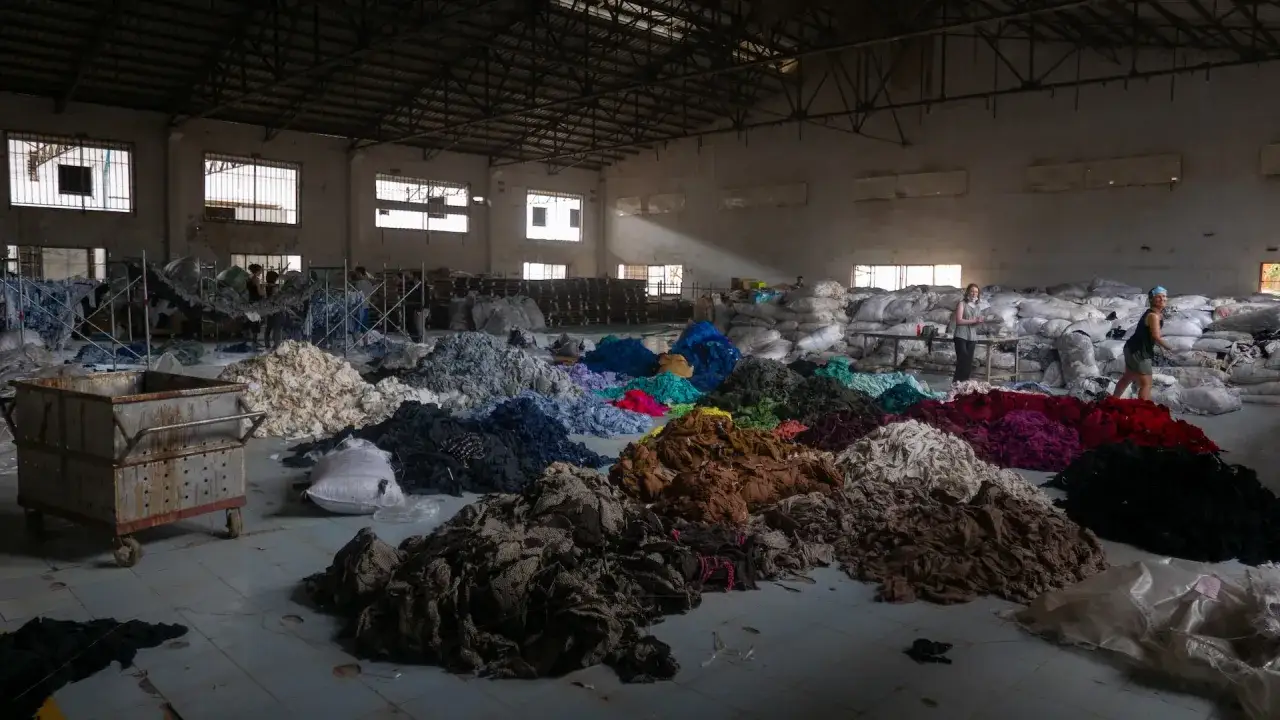 Montones de textiles de colores en un almacén, reflejo de las fast fashion consecuencias.