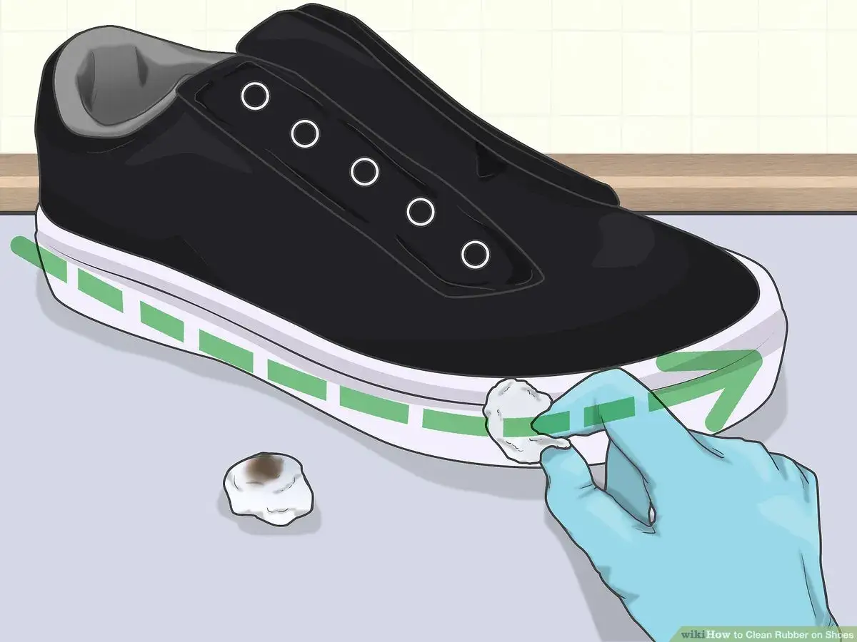 Guante azul limpia la goma blanca de una zapatilla negra, mostrando cómo limpiar las gomas de las zapatillas.
