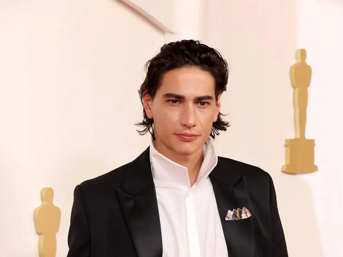 Enzo Vogrinčić, con traje negro y camisa blanca, posa con un broche colorido en la solapa.