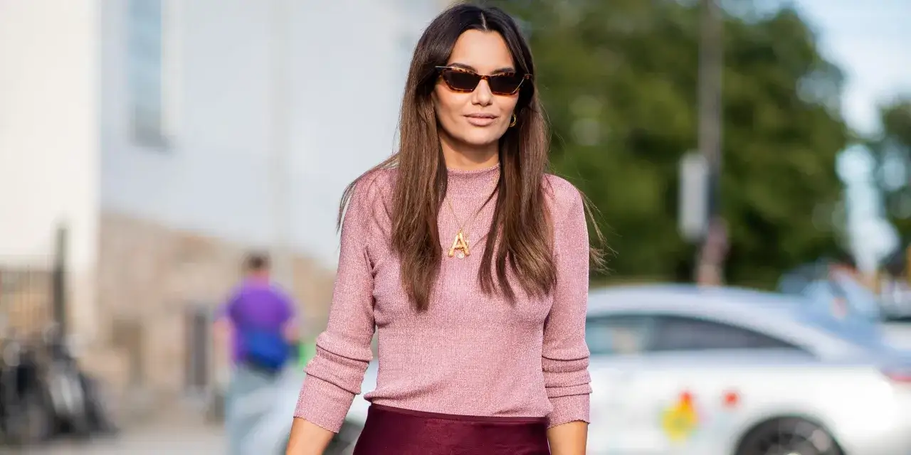 Mujer con gafas de sol y su&eacute;ter rosa brillante, combinando granate y rosa en su atuendo.