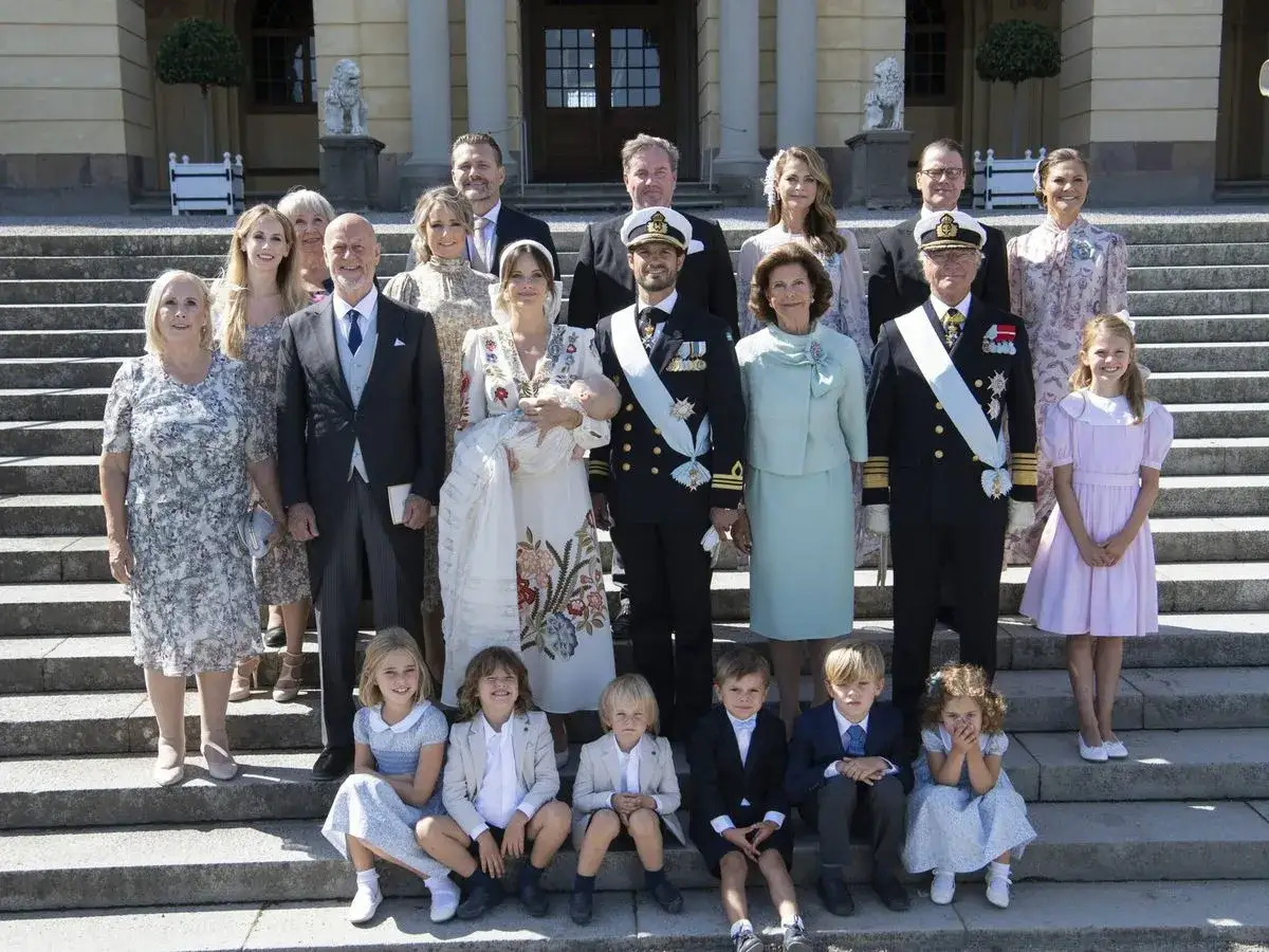 Familia real posa con el bebé en su bautizo. El outfit bautizo del bebé es un traje blanco con bordados.