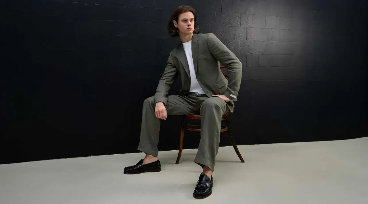 Hombre con traje de lino verde, camiseta blanca y mocasines negros. Un outfit oficina verano hombre ideal para días calurosos.