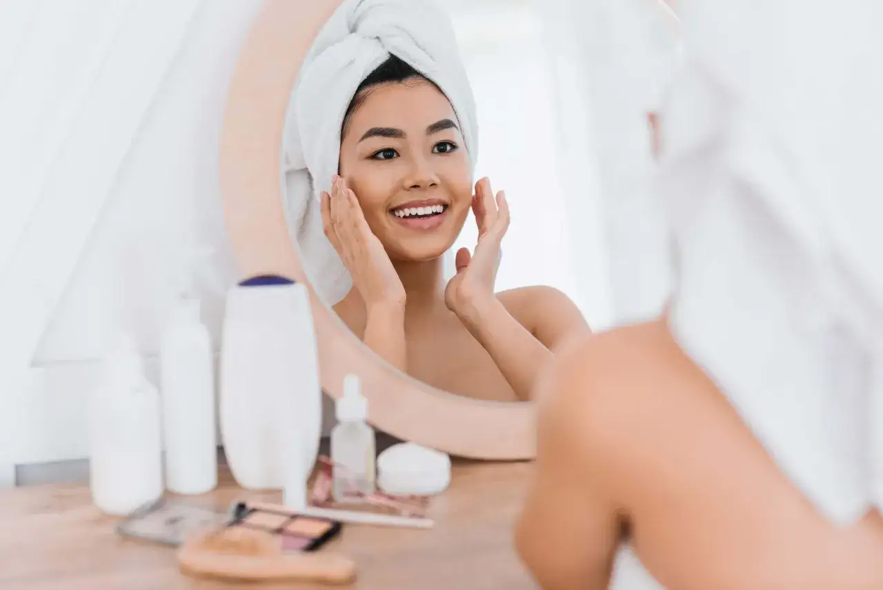 Joven sonríe mientras se toca la cara, disfrutando de su rutina de limpieza facial.