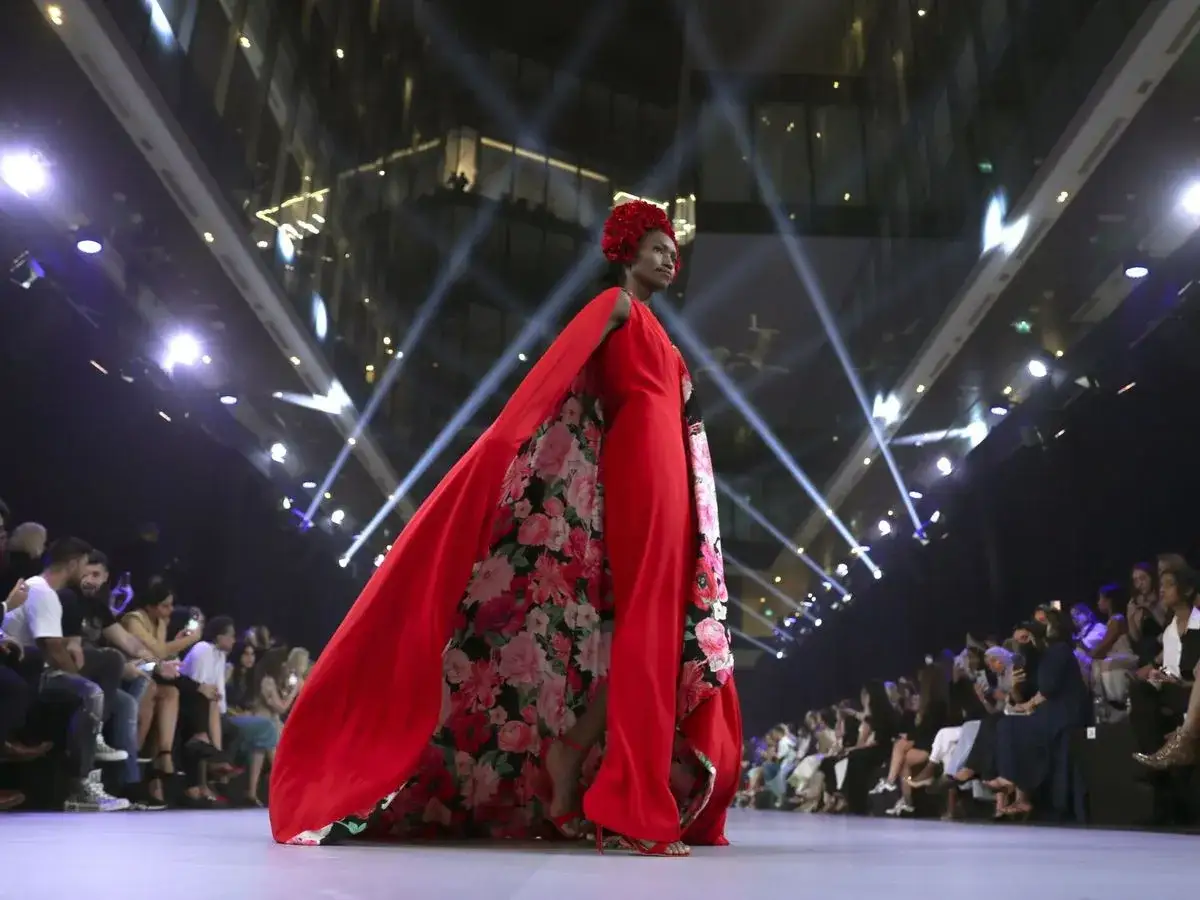 Una modelo luce un espectacular vestido rojo con capa y estampado floral, evocando la audacia de Alessandro Michele en la pasarela.