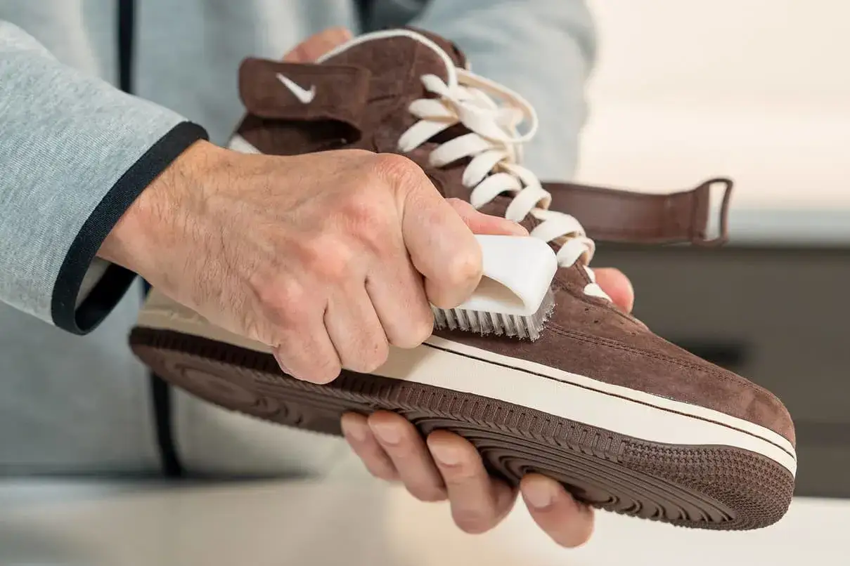 Man limpiando un zapato de ante marrón con un cepillo blanco. Aprende como limpiar zapatos de antelina para mantenerlos como nuevos.