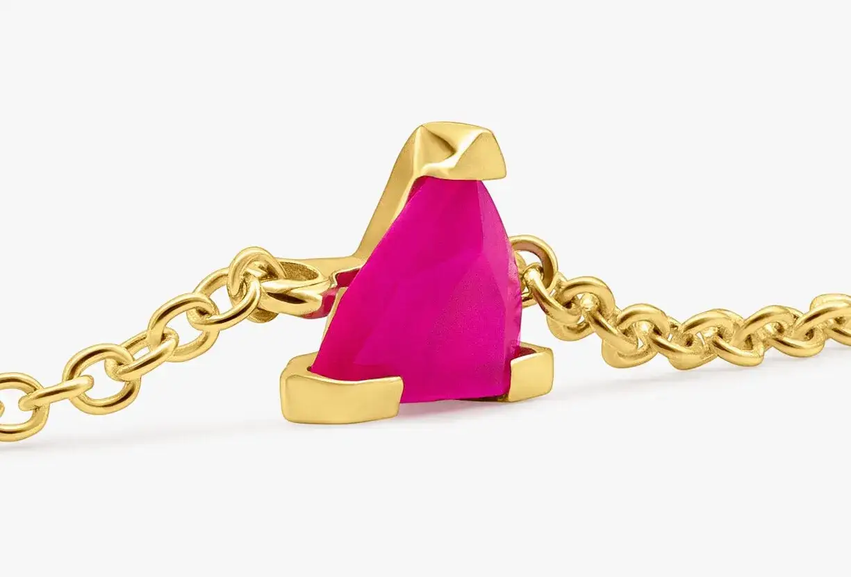 Un delicado collar de oro con un vibrante cristal rosa, capturado en un suot studio.