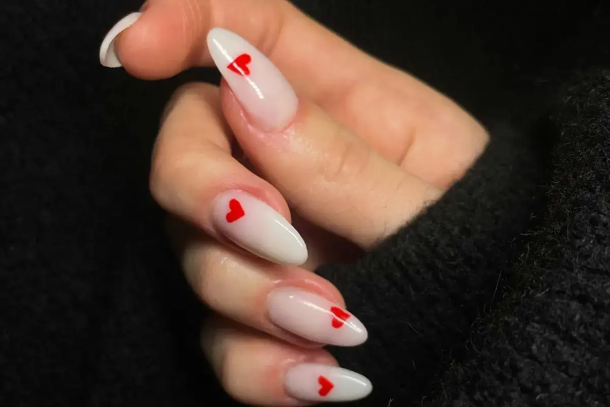 Uñas blancas con corazones rojos, perfectas para San Valentín 2026.