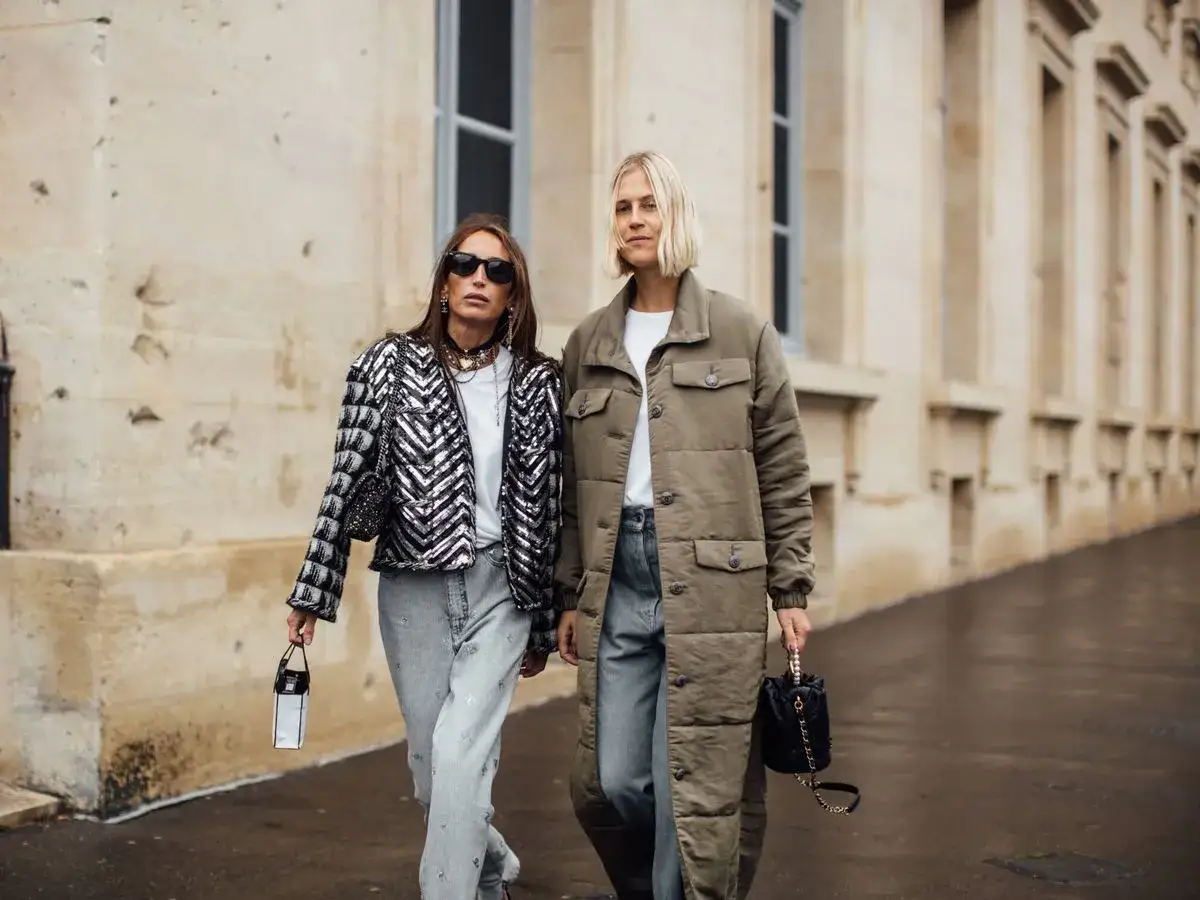 Dos mujeres lucen un look elegante con vaqueros. Una lleva una chaqueta de lentejuelas y la otra un abrigo largo acolchado.