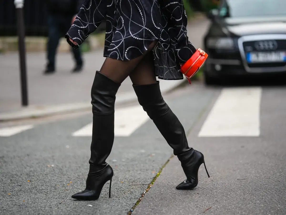 Mujer cruza la calle con un vestido estampado y se llevan las botas altas negras de tacón de aguja.