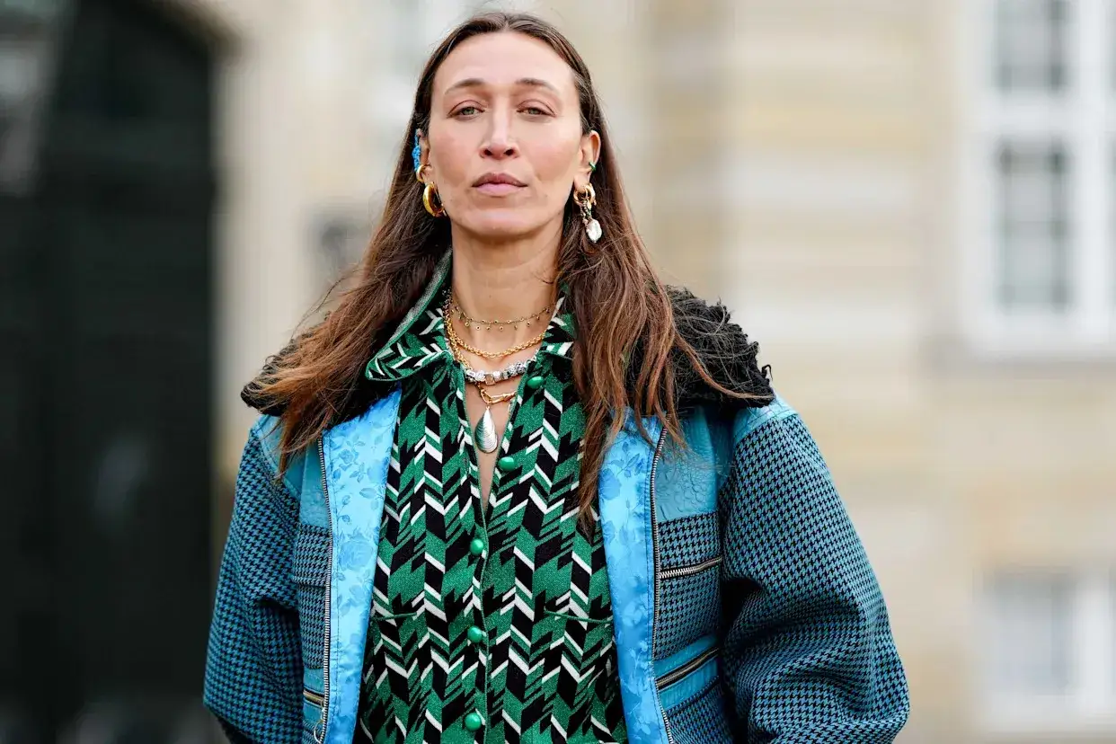 Alana Hadid luce un llamativo estampado verde y negro, con joyas doradas y un abrigo azul.