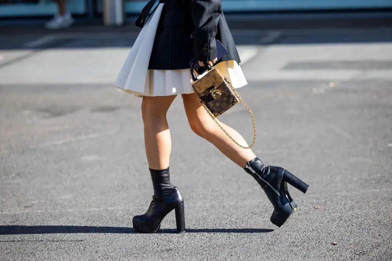 Estilos de botines: botines negros con plataforma y tacón grueso, combinados con falda plisada y bolso de diseñador.