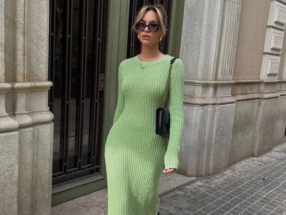Mujer con vestido de punto de color verde claro, bolso negro y gafas de sol, posando en la calle.
