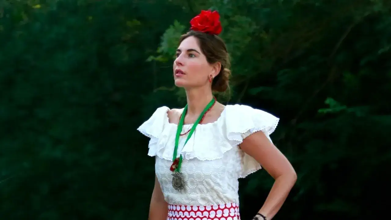 Lourdes Montes, con una rosa roja en el pelo y un vestido blanco con volantes, luce un collar verde y un cinturón de lunares rojos.