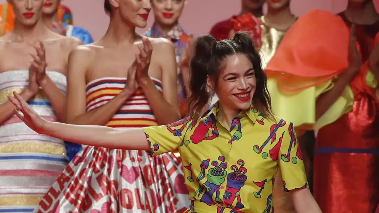 Cosima Ruiz de la Prada sonríe en un desfile, luciendo una camisa amarilla con estampado de golf y un peinado de coletas.
