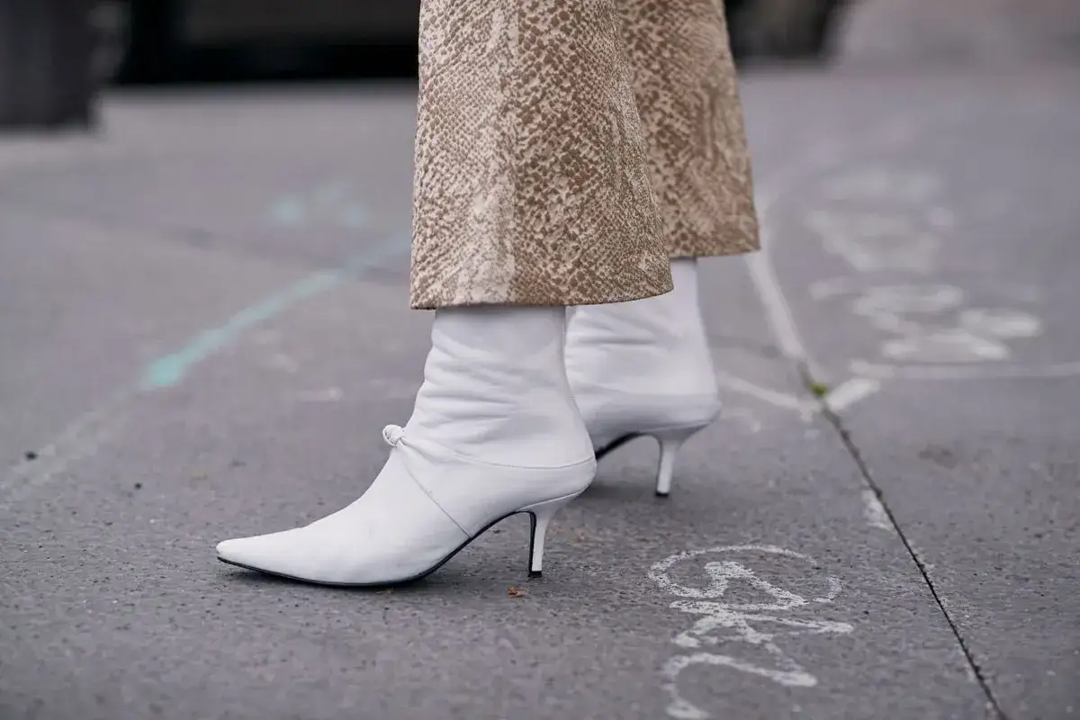 Botines blancos de tacón fino, con un detalle de lazo, combinados con pantalones de estampado serpiente. ¡Listos para limpiar y lucir!