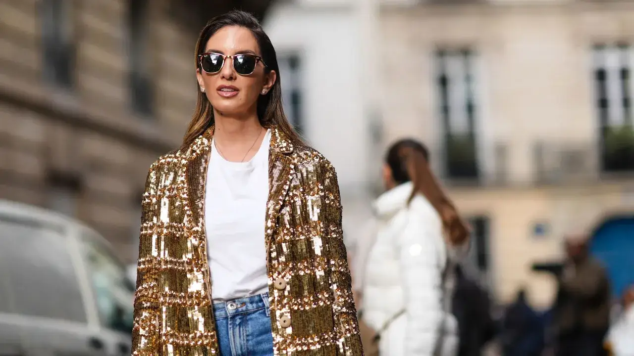 Mujer con chaqueta dorada de paillete, gafas de sol y vaqueros, lista para deslumbrar.