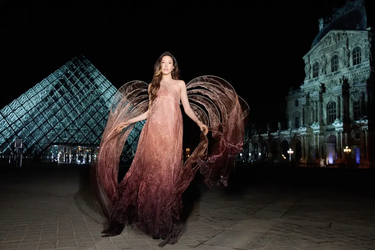 Eileen Gu, como un ángel etéreo, posa frente a la pirámide del Louvre con un vestido vaporoso y alas translúcidas.