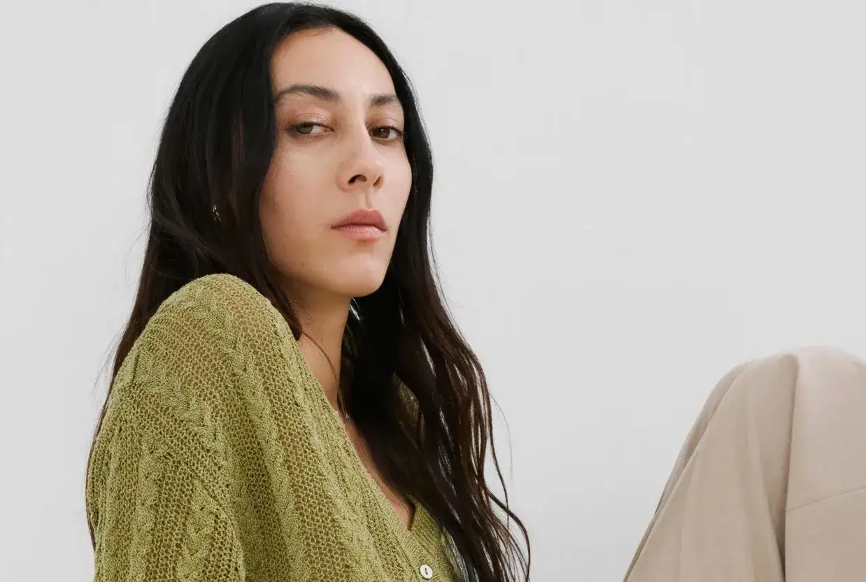 Mujer con cabello oscuro y piel clara, viste un suéter tejido de un vibrante el verde.