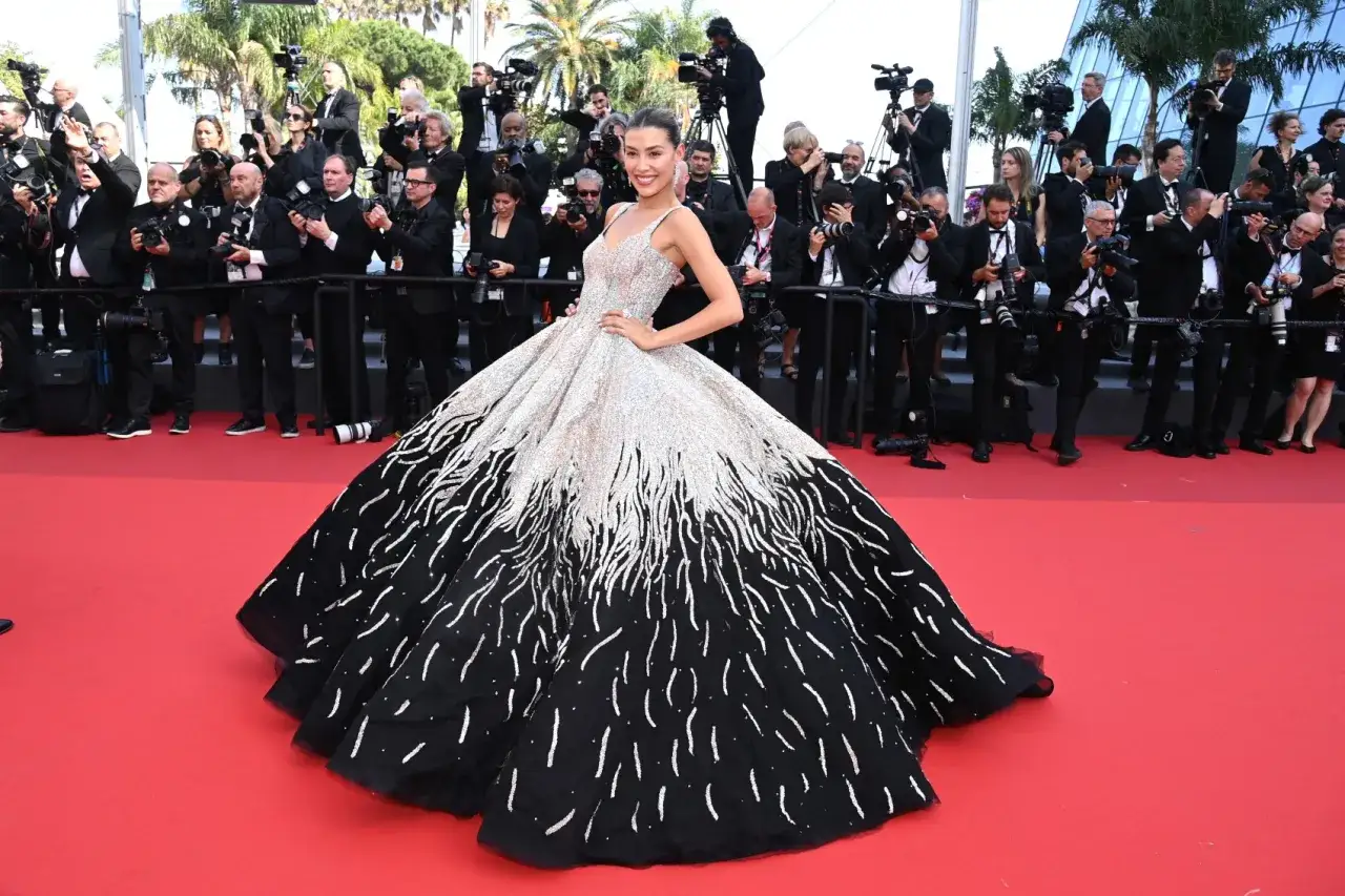 Una modelo desfila con un espectacular vestido negro y plateado en la alfombra roja de Cannes, rodeada de fotógrafos.
