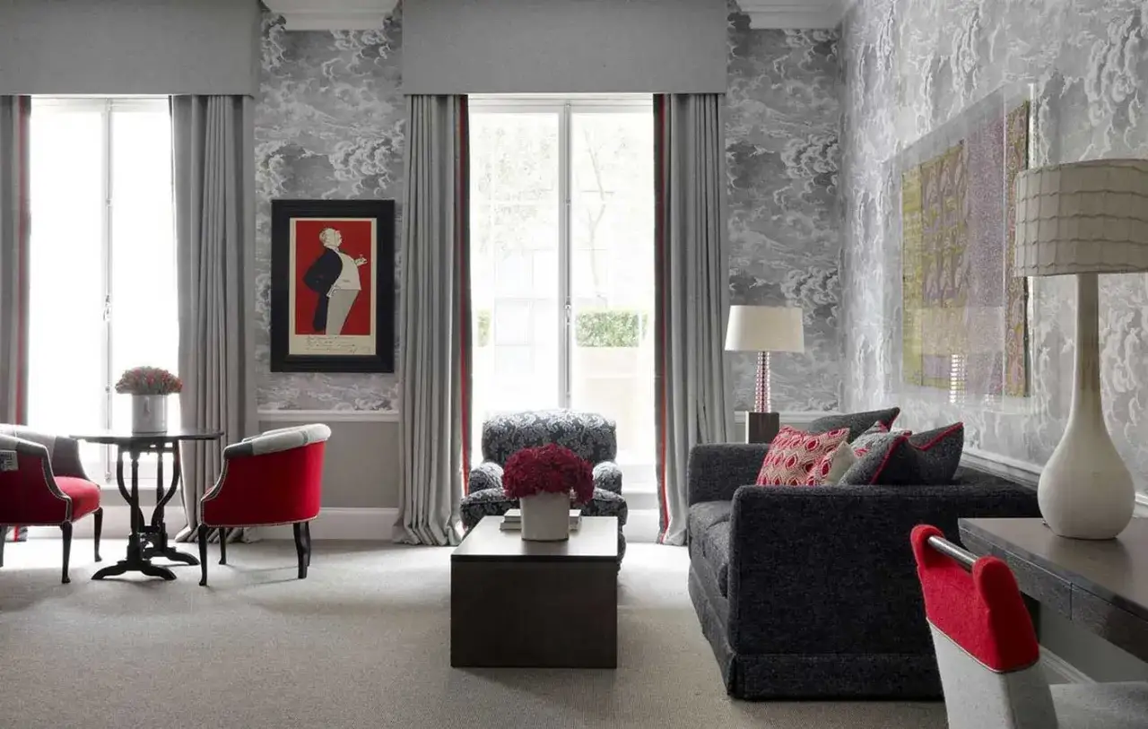 Elegante salón con paredes grises y detalles en rojo vibrante. Sofá oscuro, sillones rojos y un cuadro de un hombre con traje. Los colores que combinan con el gris resaltan en esta estancia.
