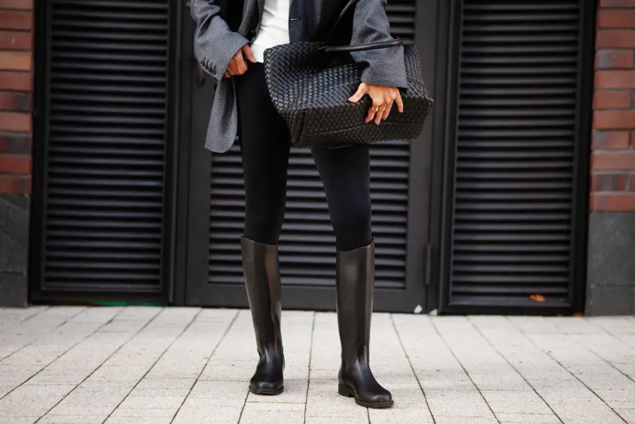 Elegante outfit con botas altas negras, chaqueta gris y bolso tejido.