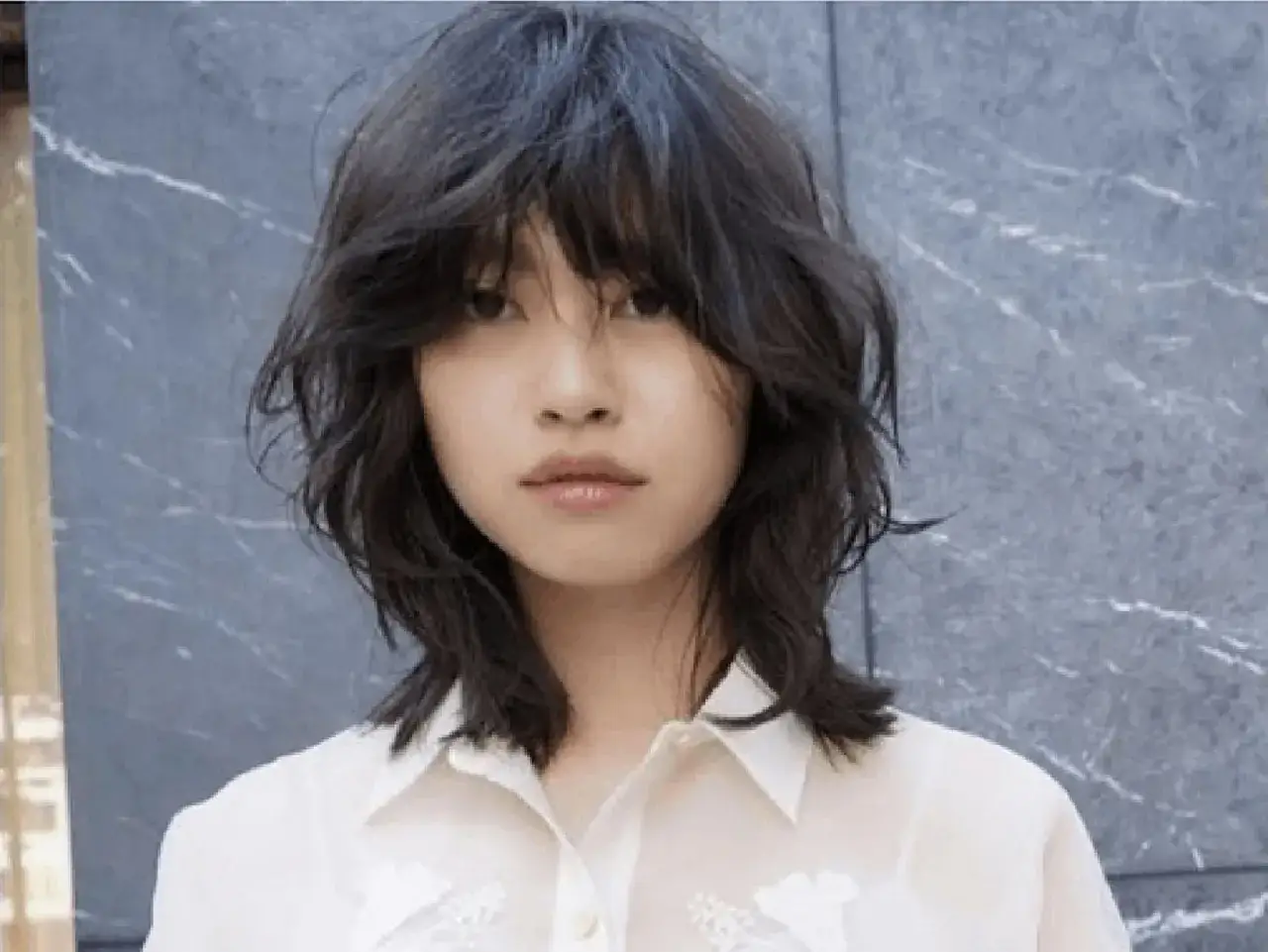 Mujer joven con un corte de pelo wolf cut desordenado y moderno, con capas que enmarcan su rostro.