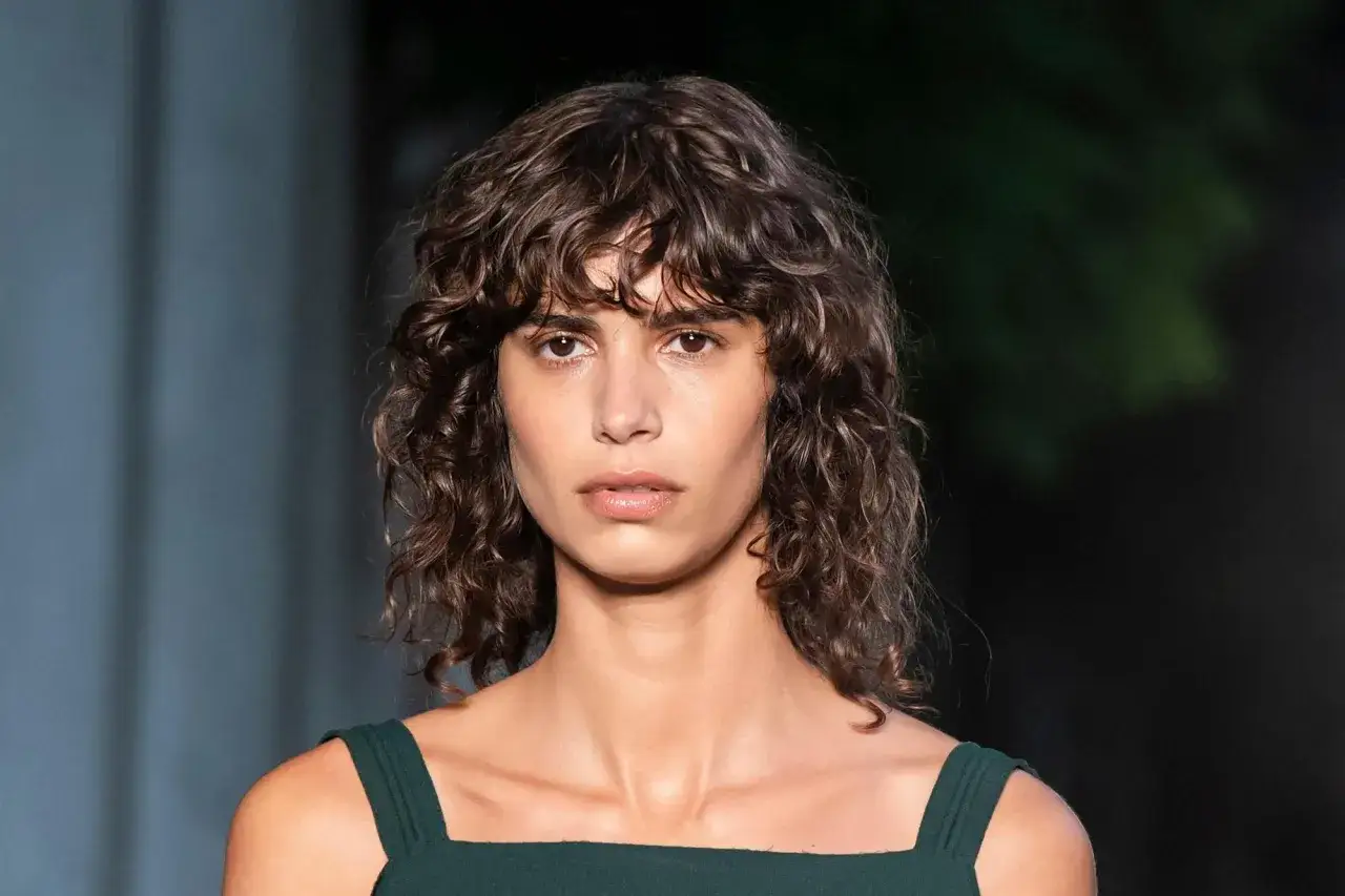 Mujer con flequillo cortina y pelo rizado, luciendo un vestido verde oscuro.