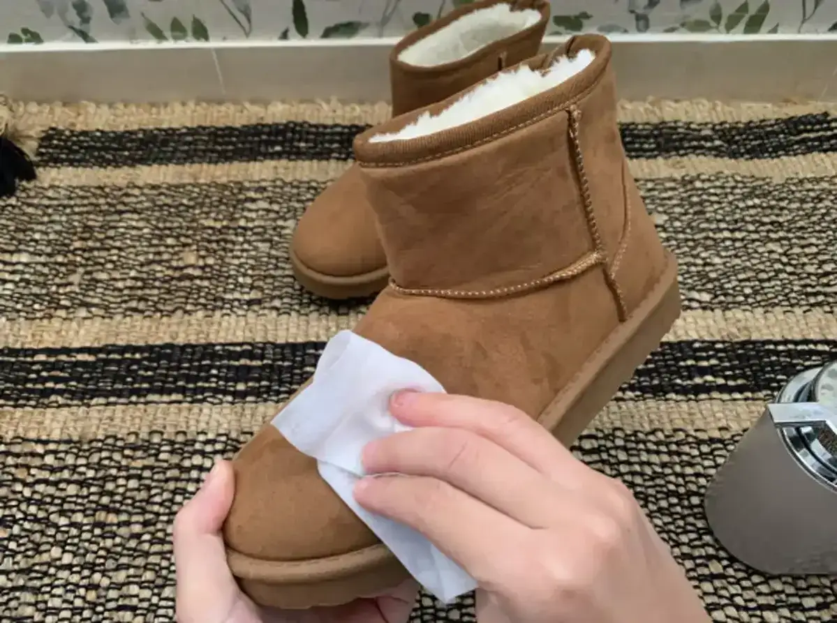Manos limpiando unas botas de serraje beige con un paño húmedo. Aprende cómo limpiar botas serraje beige para que queden como nuevas.