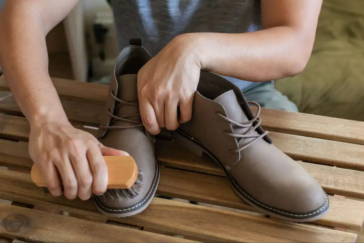 Man cepilla unas botas de cuero marrón. Aprende como limpiar unas botas para mantenerlas como nuevas.