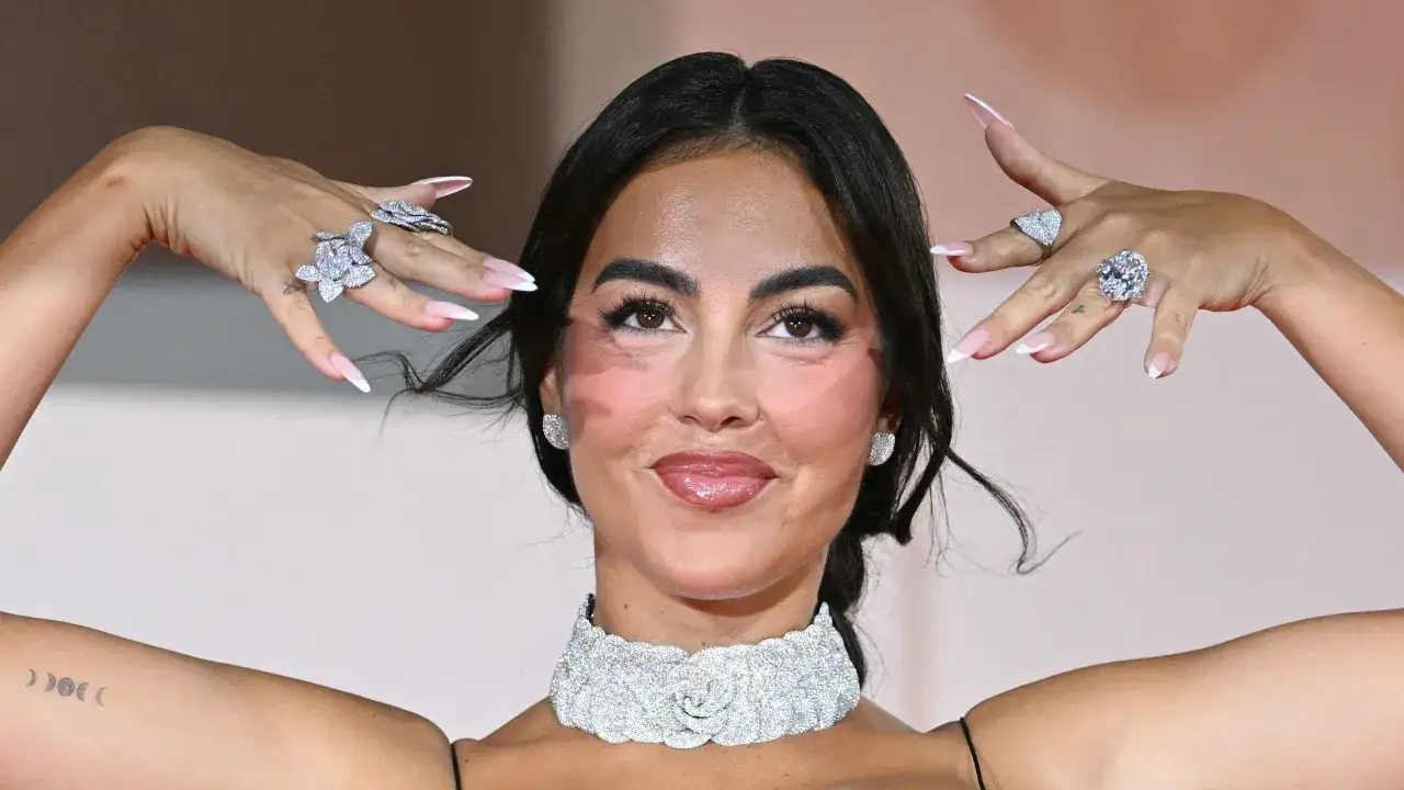 Georgina luce un deslumbrante anillo y un collar de diamantes, con uñas impecables y un maquillaje radiante.