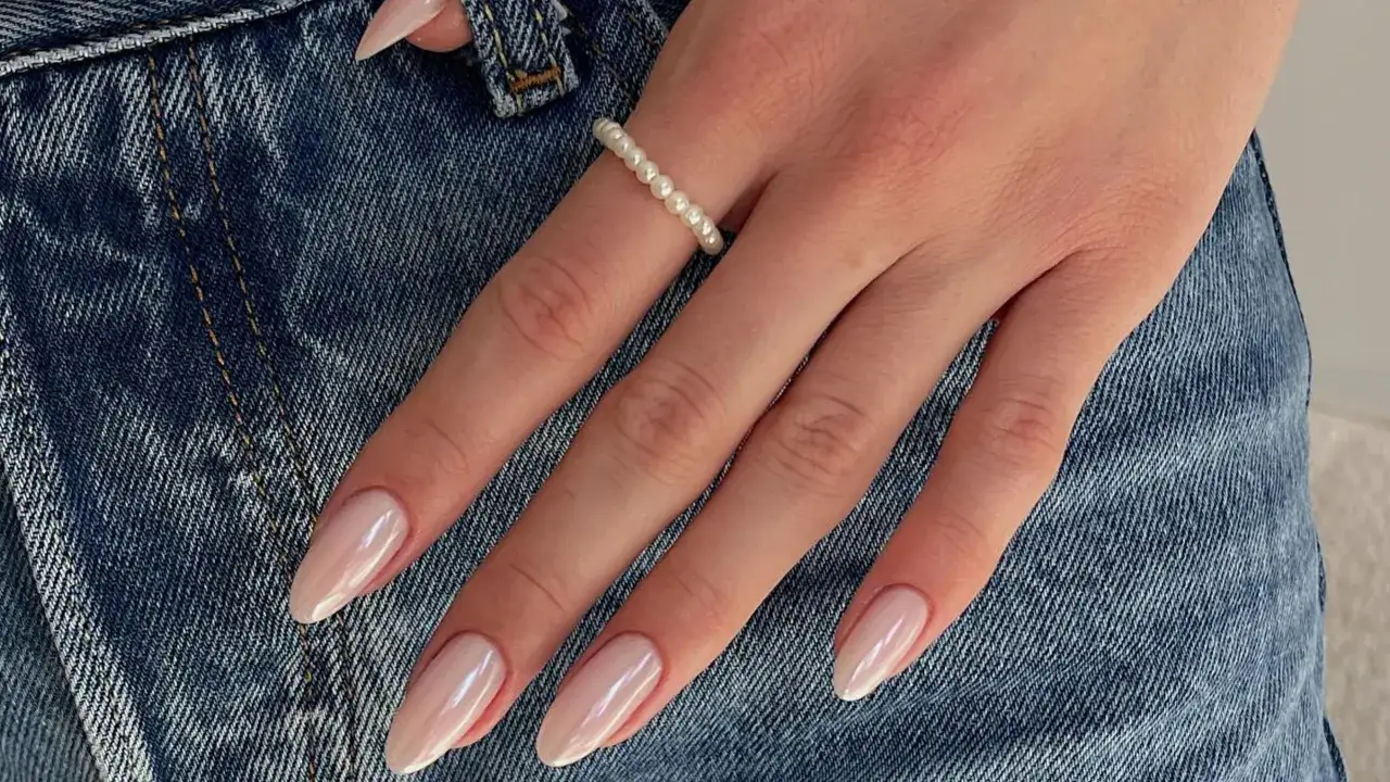 Manos con uñas nude almendradas, un anillo de perlas y vaqueros.