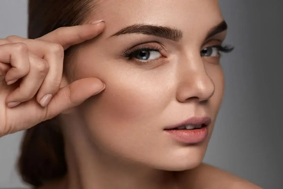 Primer plano de una mujer con cejas perfectas, su mano acaricia su rostro.