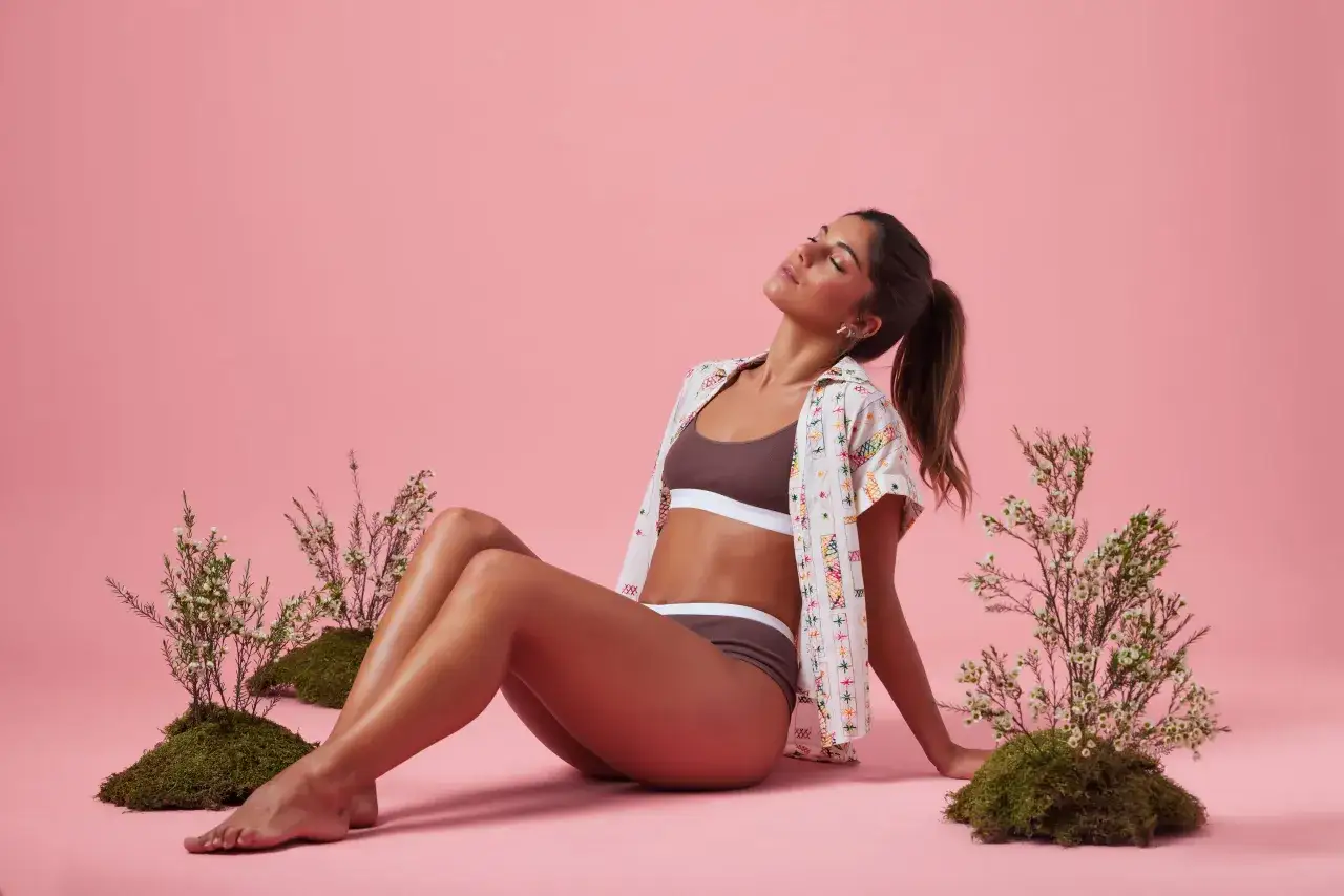 Sara Baceiredo, con los ojos cerrados, disfruta de un momento de paz rodeada de naturaleza y un fondo rosa.