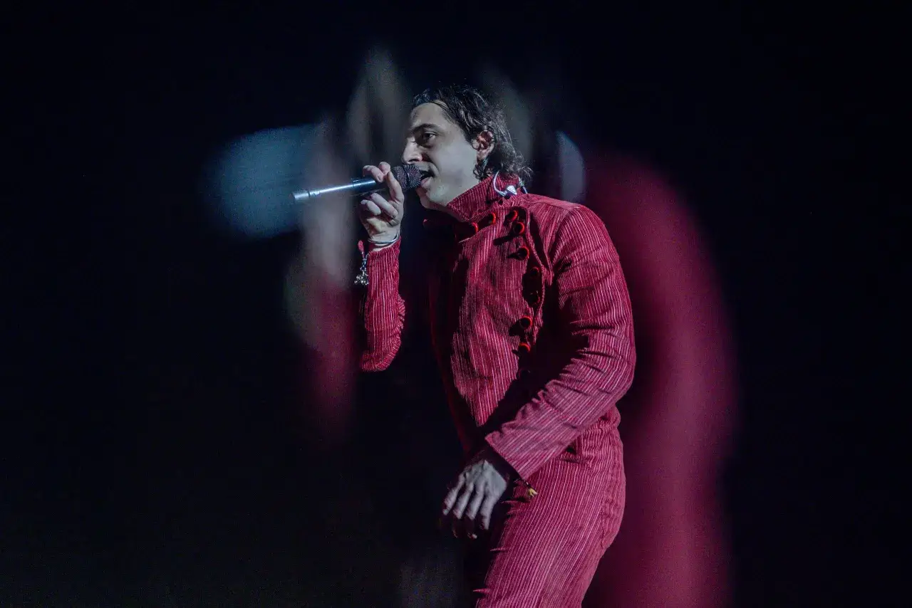 Ralphie Choo, con su traje rojo a rayas, canta apasionadamente en el escenario, iluminado por luces tenues.