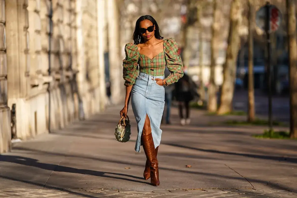 Mujer con outfit falda vaquera larga, top de cuadros y botas altas.