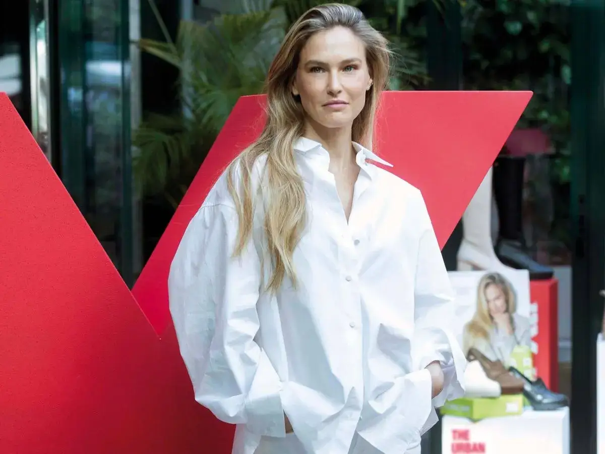 Mishel Gerzig, con su cabello rubio suelto y una camisa blanca oversize, posa frente a un gran diseño rojo.