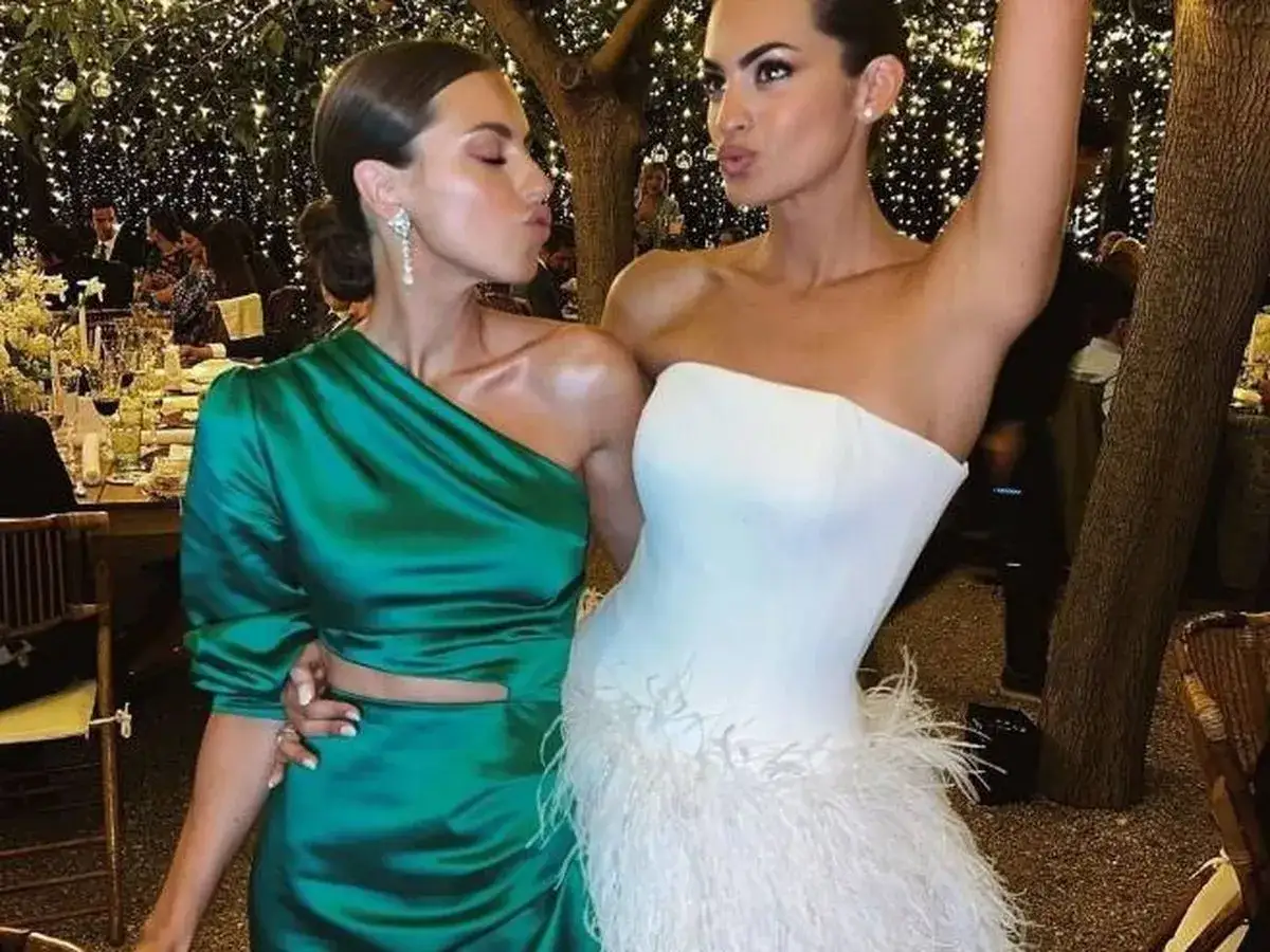 Marta Lozano y amiga, vestidas de fiesta, se preparan para celebrar una boda bajo luces festivas.