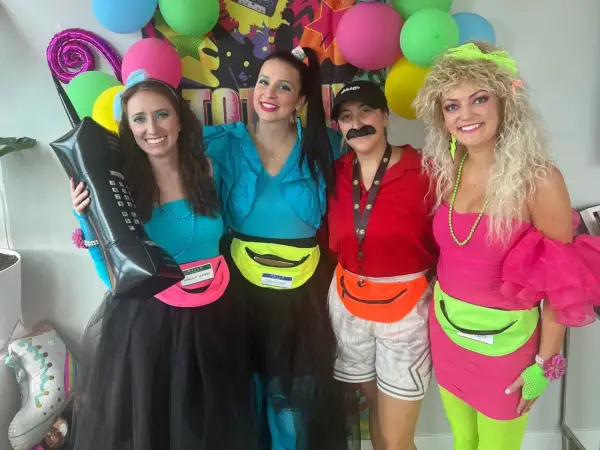 Cuatro amigas celebran una fiesta moda de los 80 con atuendos coloridos, riñoneras y peinados voluminosos.